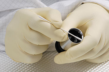 Gloved hands swabbing a small machine part